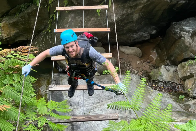 Climber in a helmet and harness crossing a via ferrata suspension bridge over the river in El Yunque