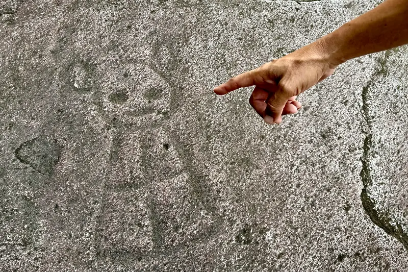 Guide pointing at a Taino petroglyph carved into a river boulder at Charco El Hippie