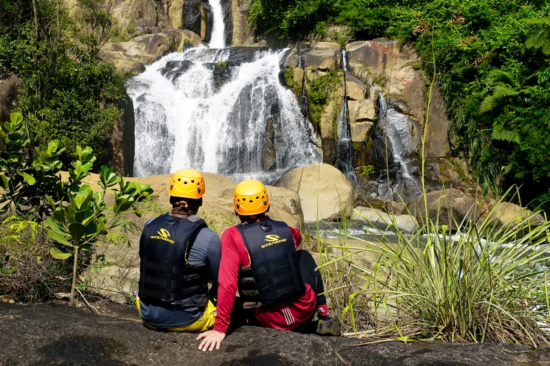 Two hikers seated in front of twin waterfalls on a private river, south side of El Yunque