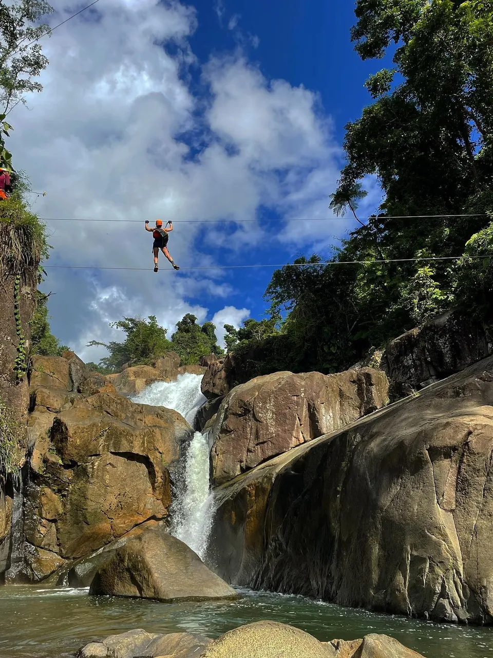 Guest crossing a cable line strung high above a waterfall canyon in El Yunque