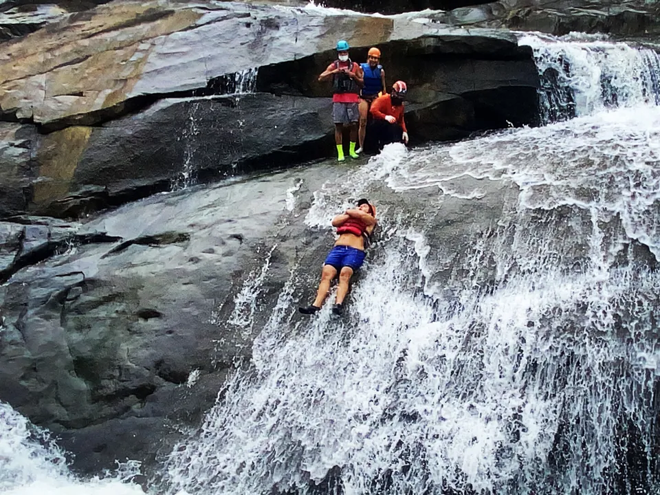 Two guests sliding a rock chute into a rainforest pool on the south side of El Yunque