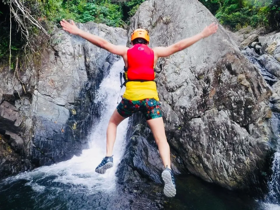 Guest leaping from a rock ledge beside a waterfall into a rainforest pool, El Yunque