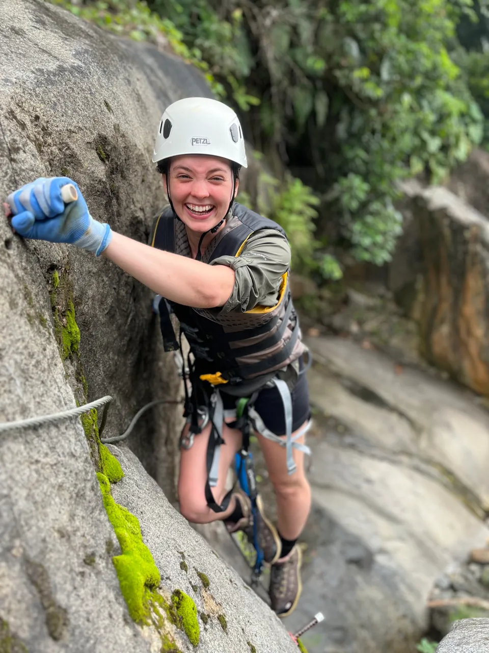 Climber in a helmet and harness gripping the steel cable and iron rungs on the via ferrata rock face, south side of El Yunque