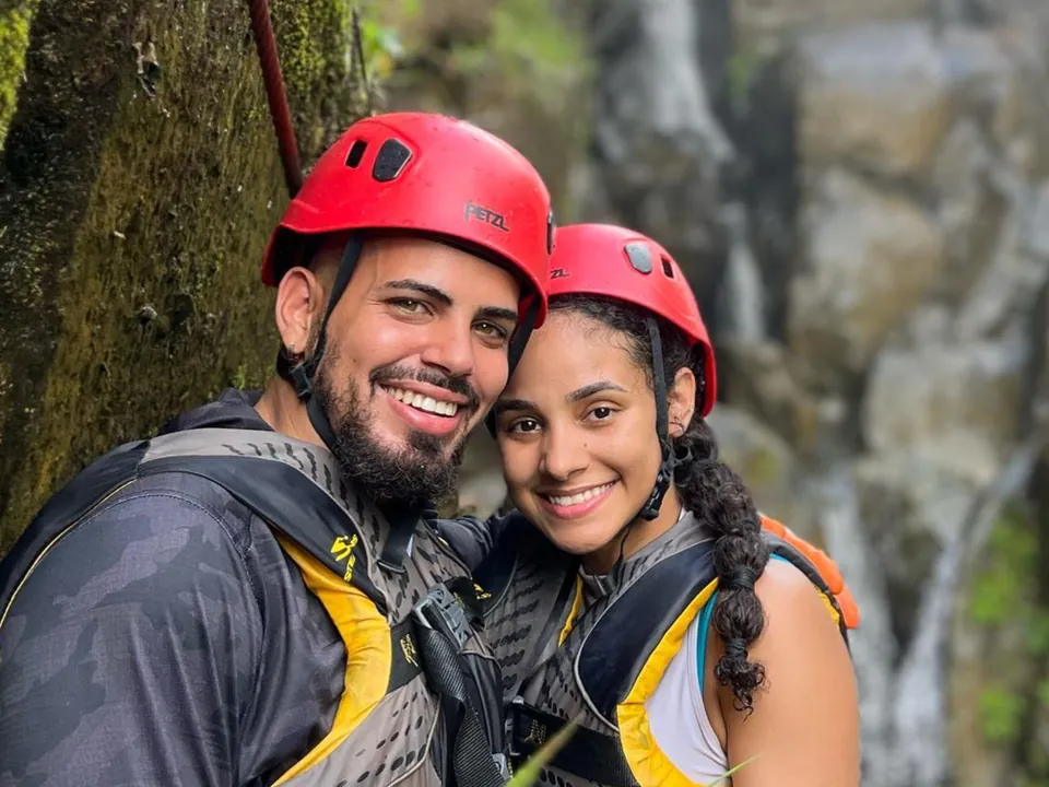 Couple in climbing helmets and harnesses with a waterfall behind them on the south side of El Yunque