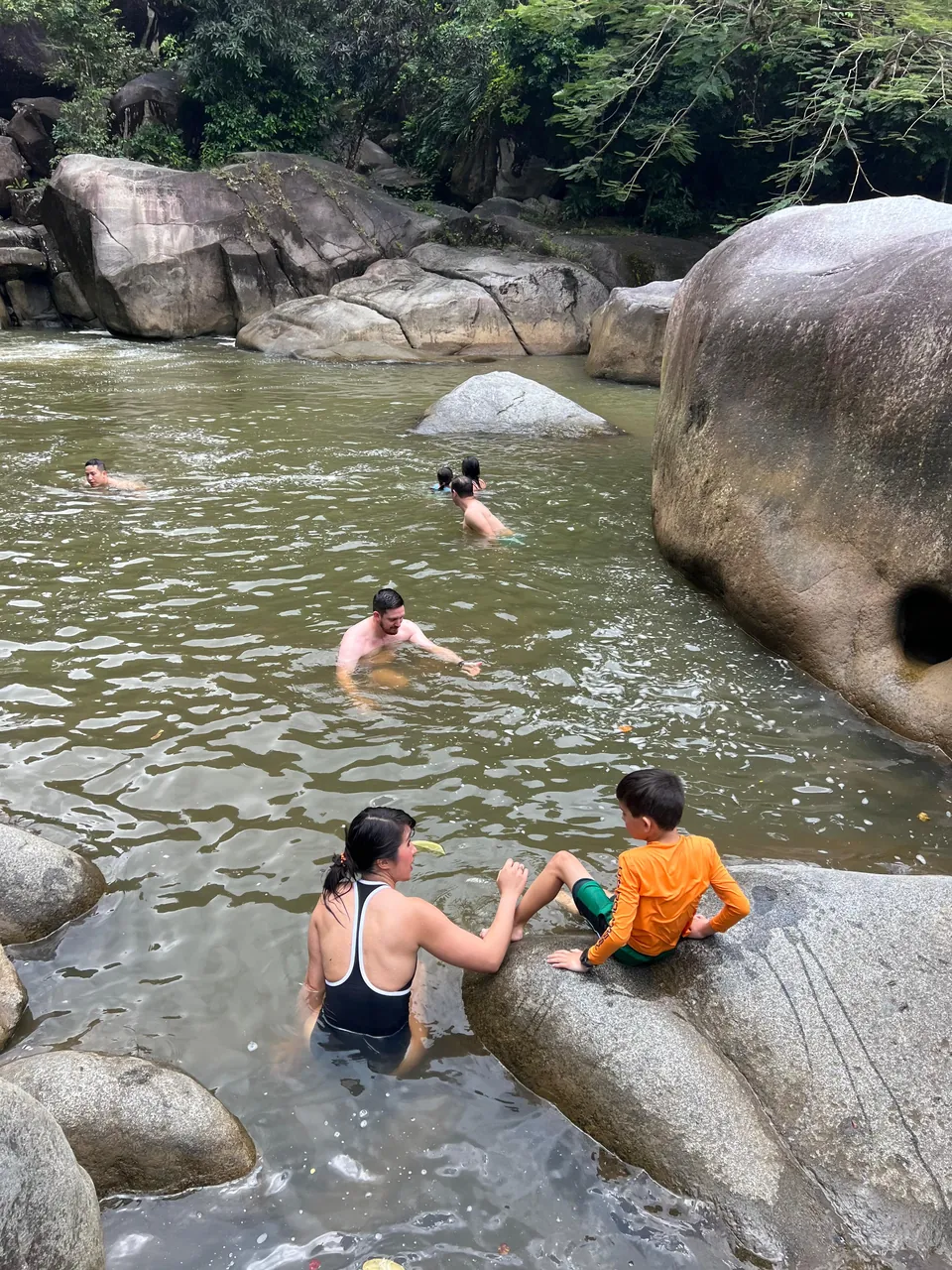 Parent and child sitting in a natural pool between boulders at Charco El Hippie