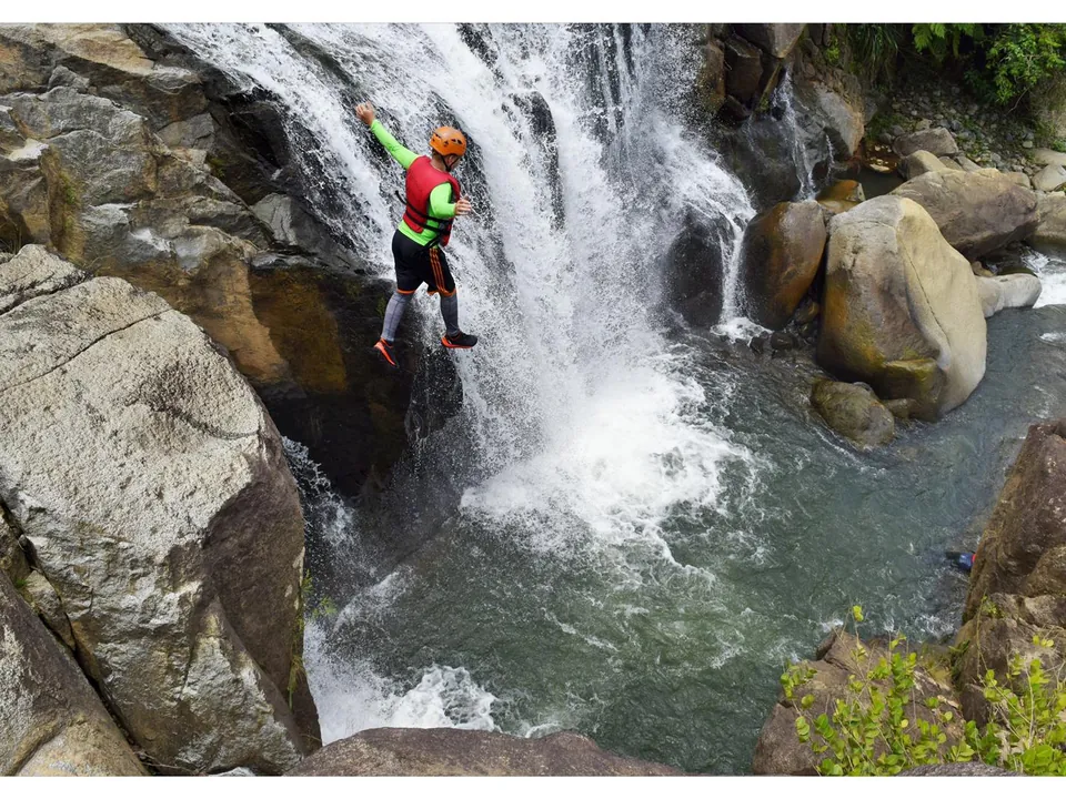 Hiker in a helmet climbing down beside a waterfall into a boulder pool in El Yunque